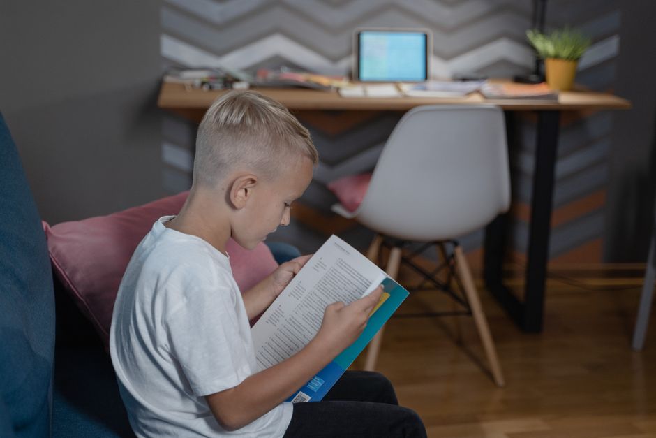 A child focused on reading a book indoors at home, promoting study and concentration.