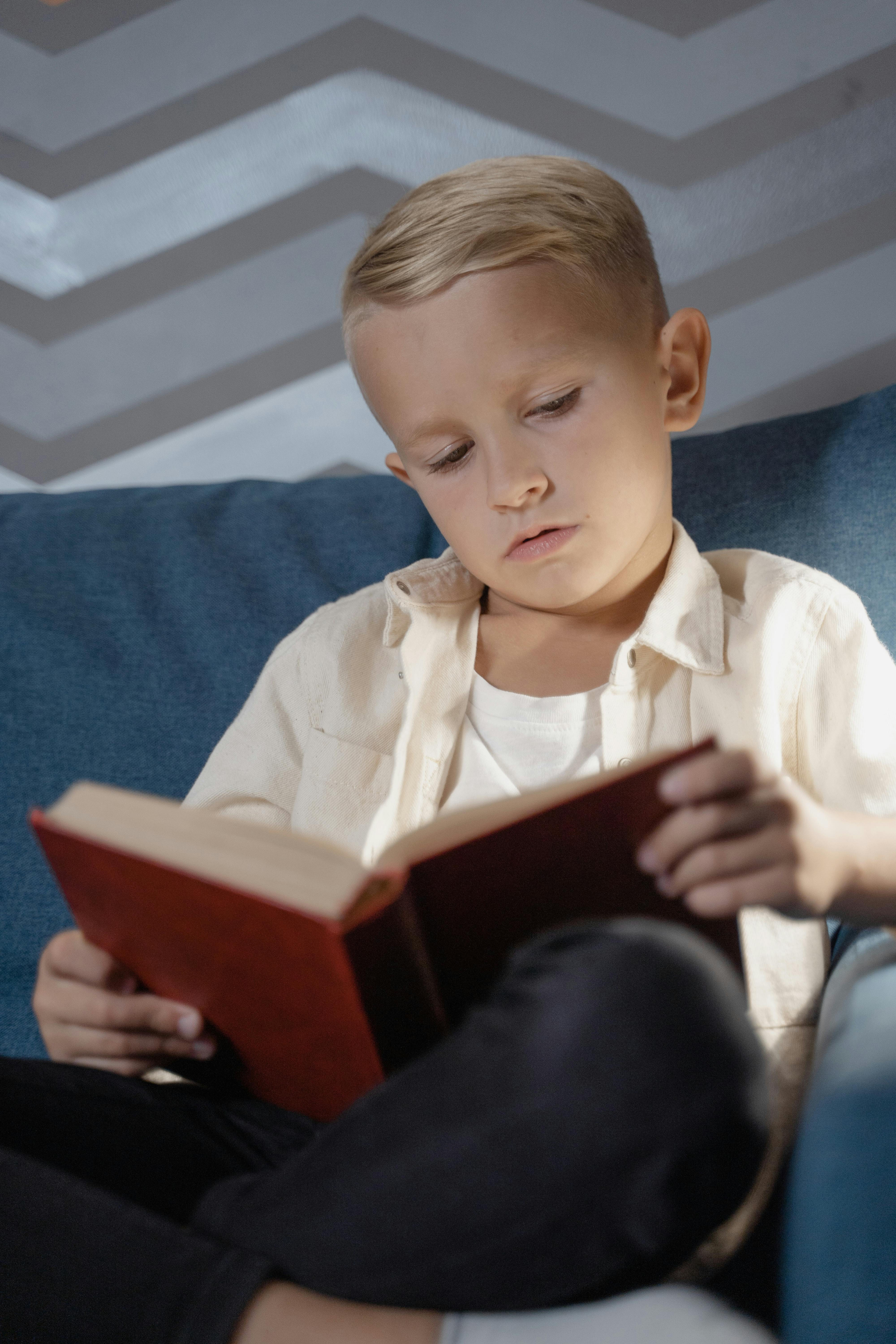 a boy sitting on a couch while reading a book