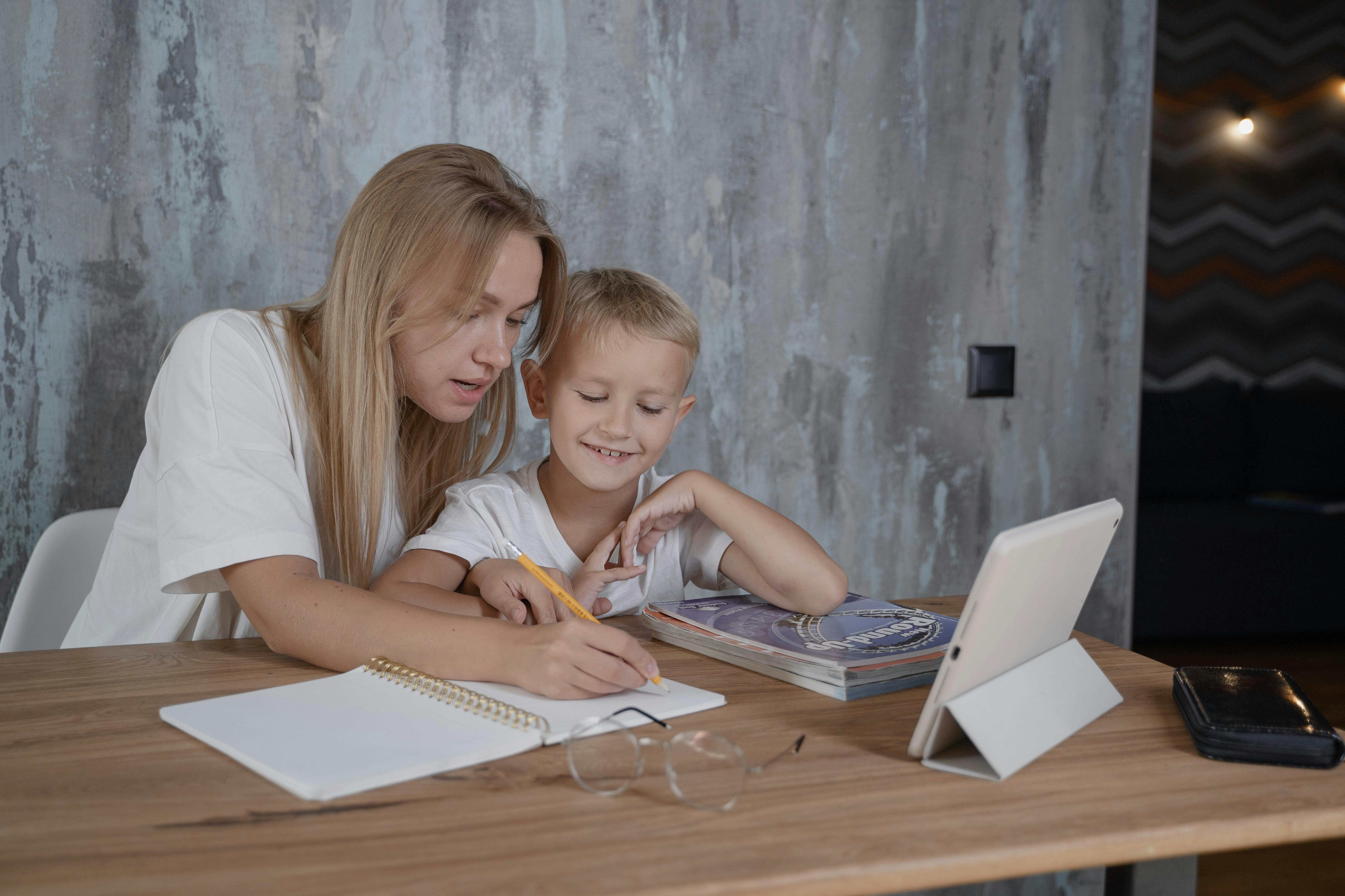 a woman writing on a notebook while sitting beside a boy