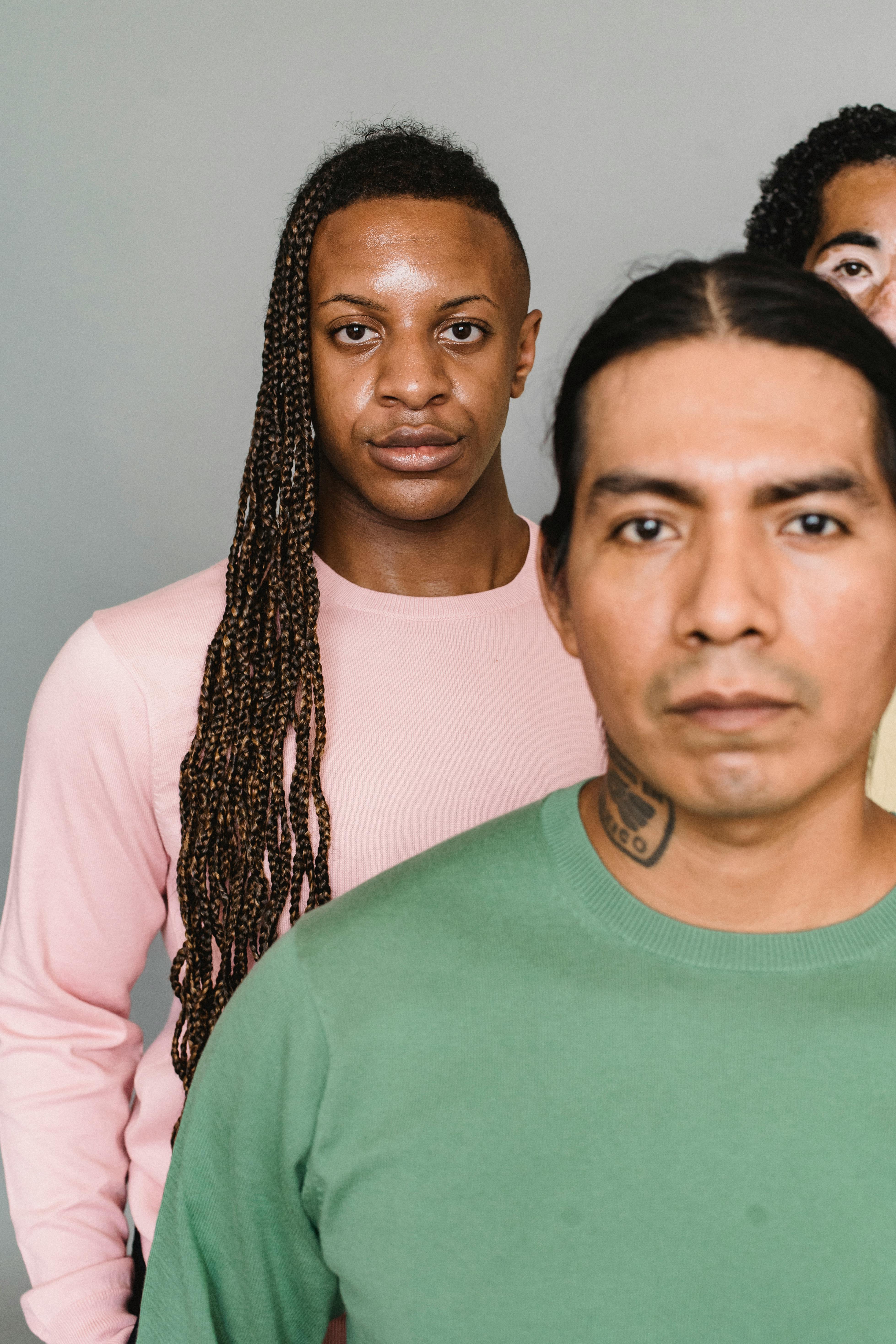 Group of multiethnic male models in trendy outfits standing against gray background and looking at camera