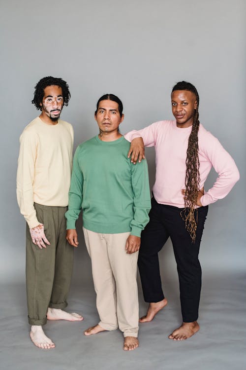 Full length of diverse barefoot male models in stylish clothes standing close and looking at camera against gray background