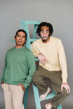 多位穿着时髦、自信的多种族男模特坐在灰色背景前的梯子上，注视着镜头