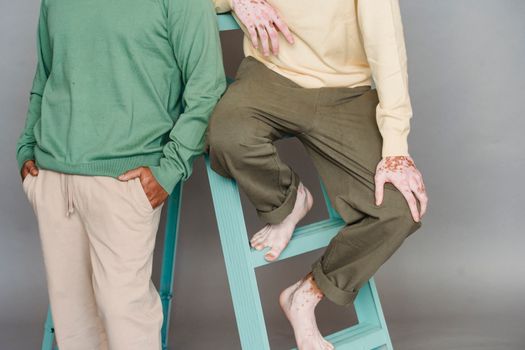 一名无法辨认的男性模特穿着时髦的衣服，靠在木梯上，背景为灰色