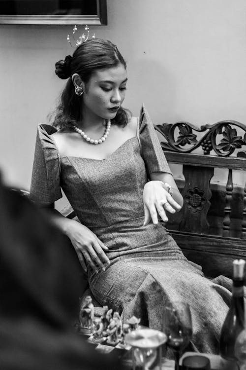 Black and white of elegant female in classy outfit sitting on bench and looking down