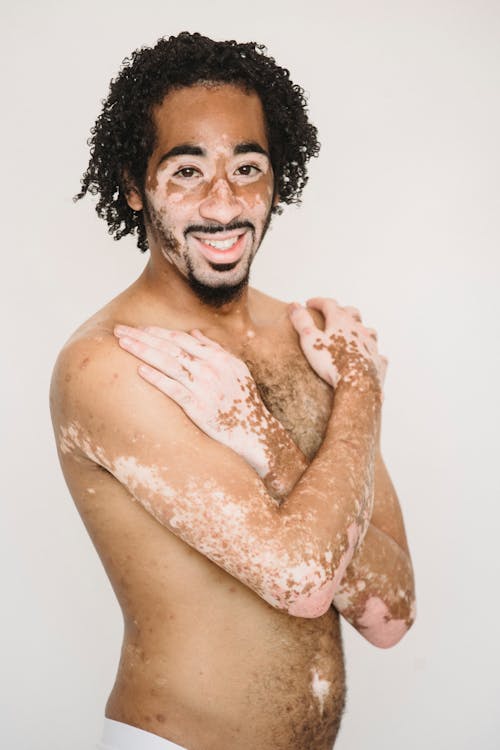 Cheerful African American male with naked torso toothy smiling while standing against white background and looking at camera