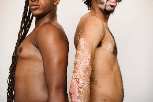 Crop ethnic men with naked torsos on light background