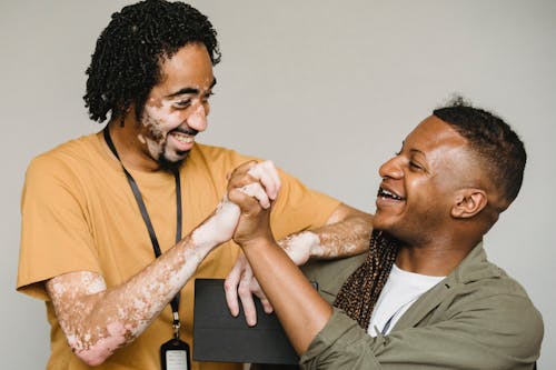 Laughing black male colleagues clasping hands in excitement together