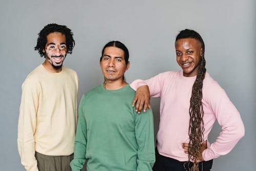 Optimistic black man living with psoriasis standing near content American Indian and homosexual black male against gray wall in photo studio