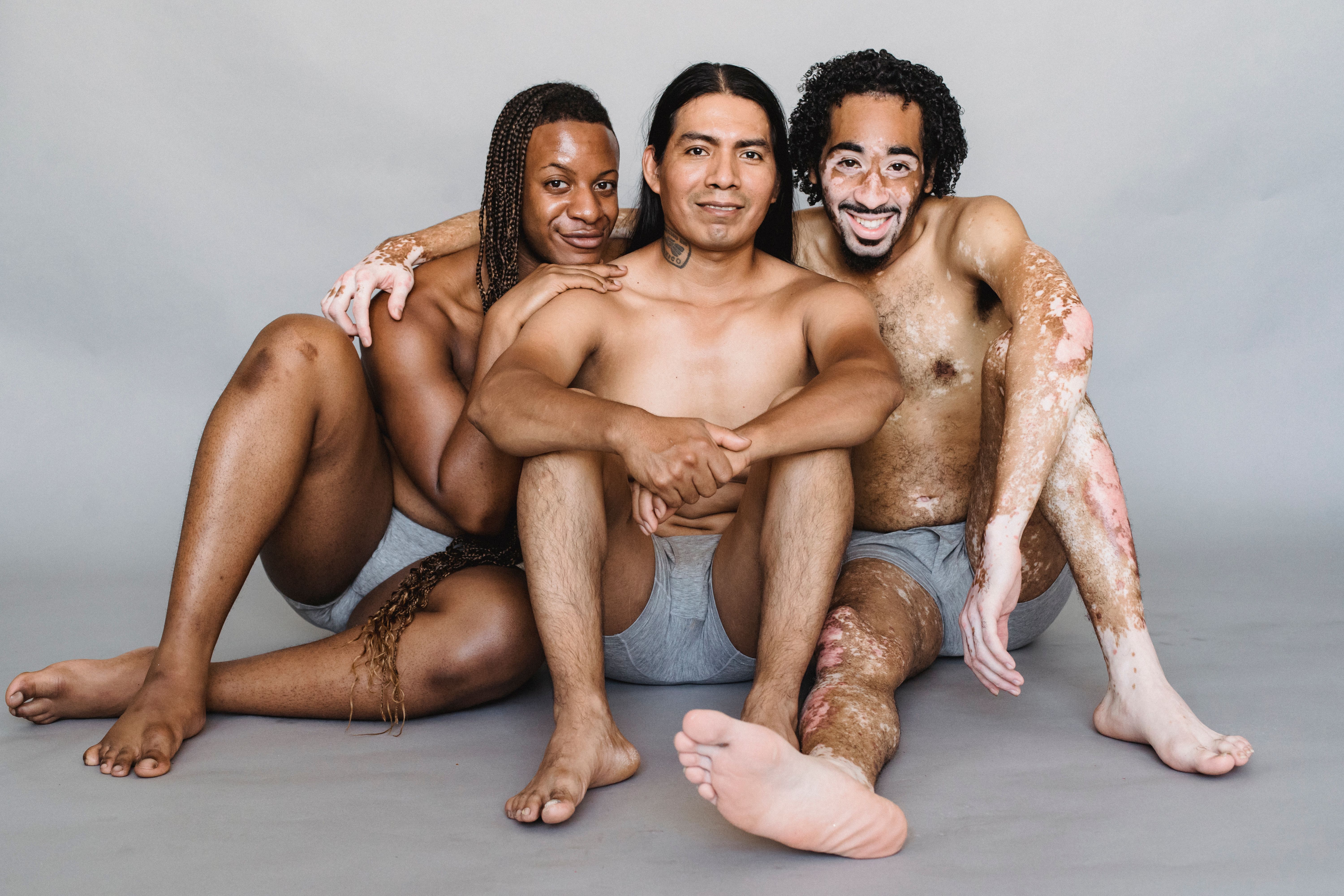 Full body of cheerful multiracial group of friends smiling and looking at camera on gray background of studio