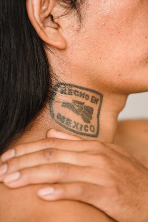 Crop anonymous ethnic man with long dark hair and tattoo on neck touching naked shoulder