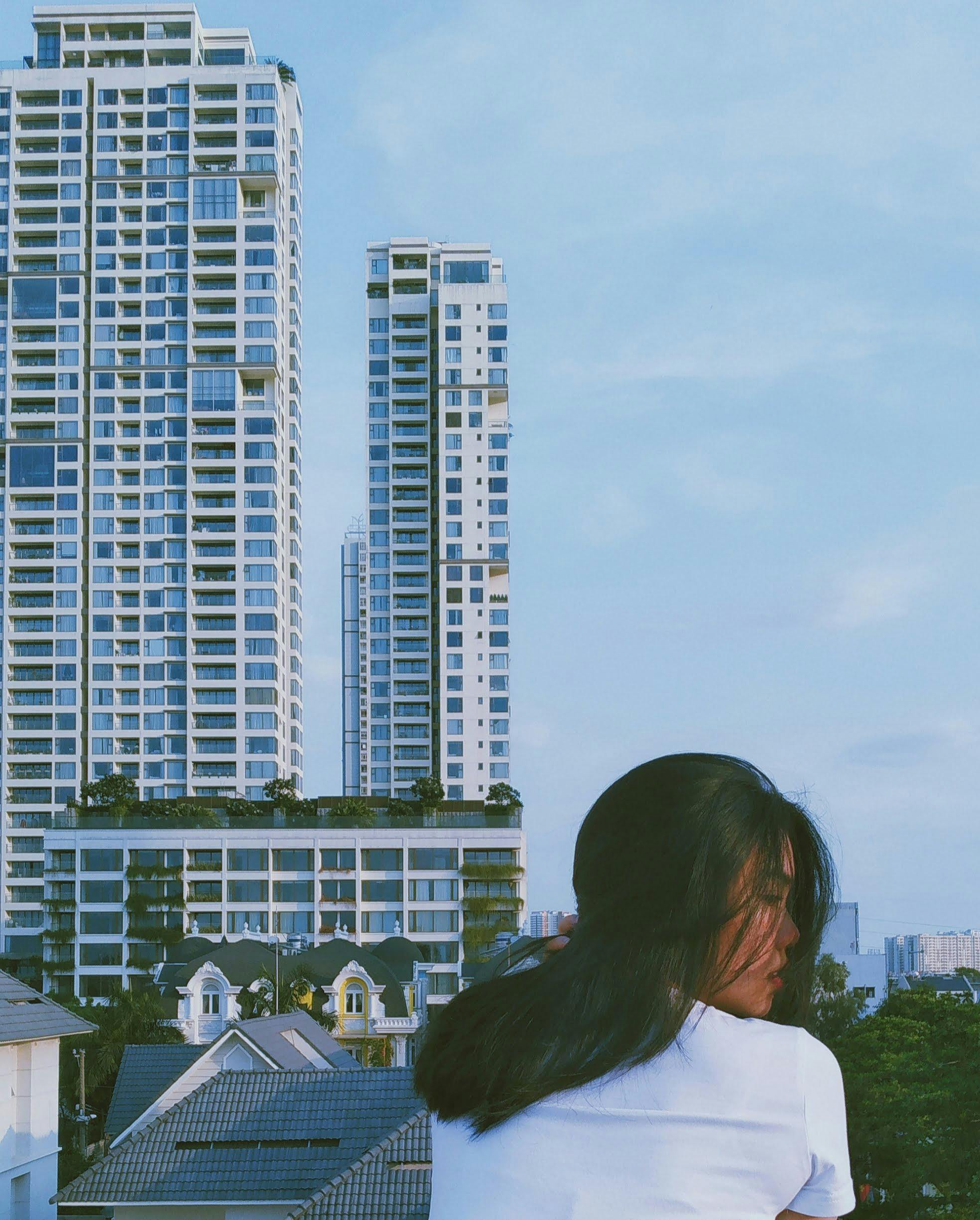 An urban cityscape featuring modern high-rise buildings in Hồ Chí Minh alongside a young woman enjoying the view.
