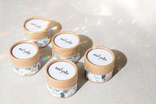 Five eco-friendly cosmetic containers with natural design in sunlight, showcasing wellness and beauty.