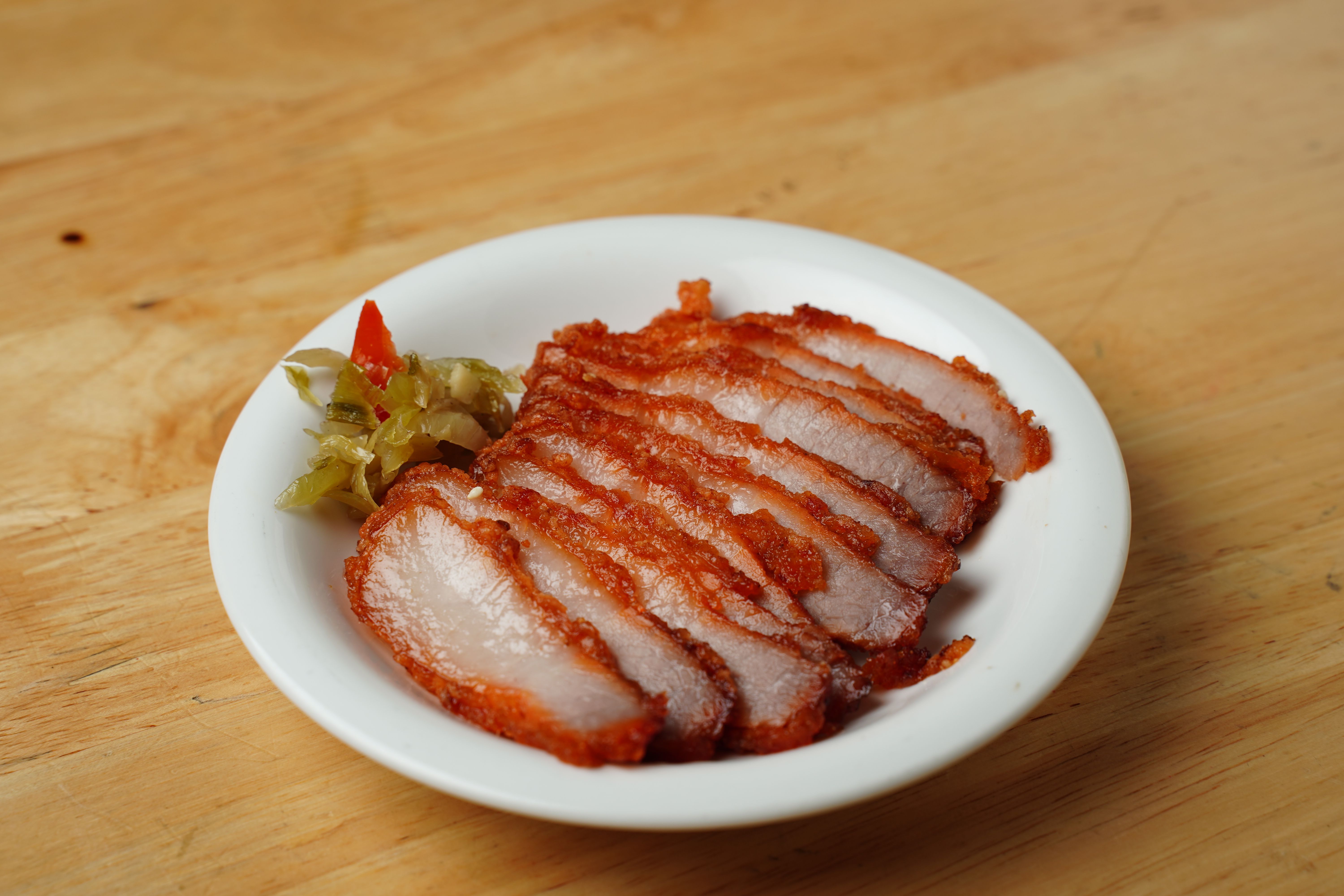 Close-up of a plated dish featuring sliced roasted pork with pickled vegetables on a wooden table.