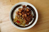 A savory bowl of braised pork with rice and vegetables on a wooden table.