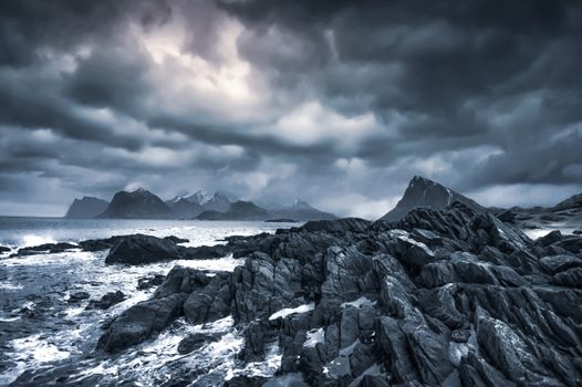 Scenic view of foamy ocean near rough mounts under gloomy sky with clouds in evening