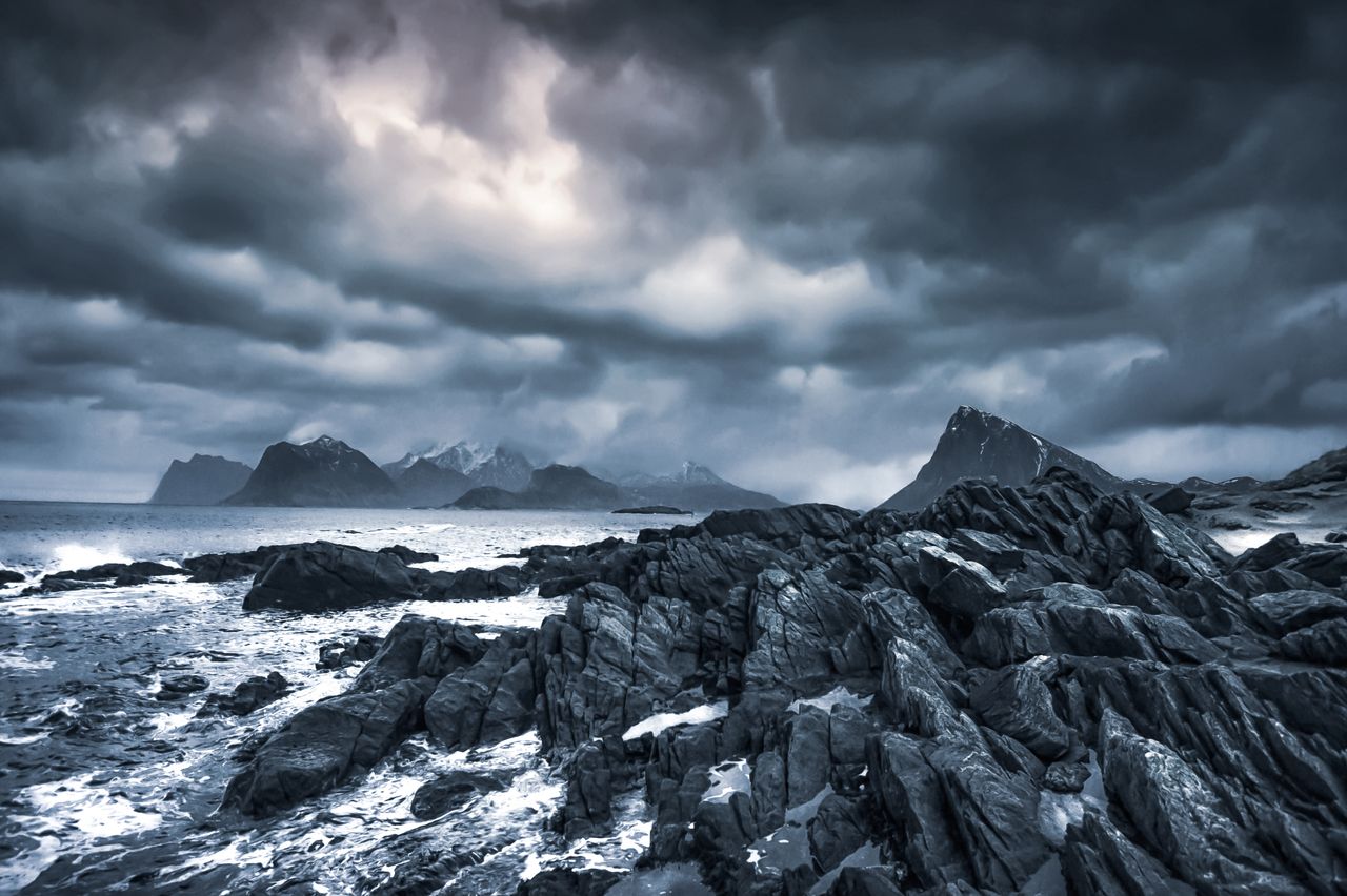 scenic view of foamy ocean near rough mounts under gloomy sky with clo