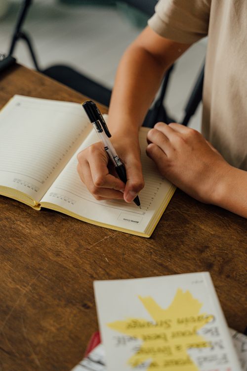 Free Close-up of a person writing in a notebook using a pen, on a wooden table. Stock Photo
