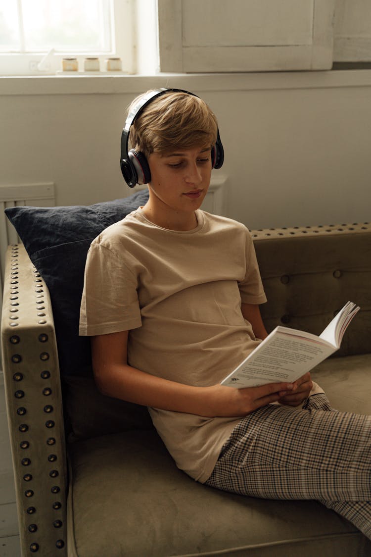 A Boy Reading A Book While Listening To Music