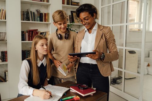 Free Students engaged in learning with a teacher using a digital tablet in a classroom setting. Stock Photo