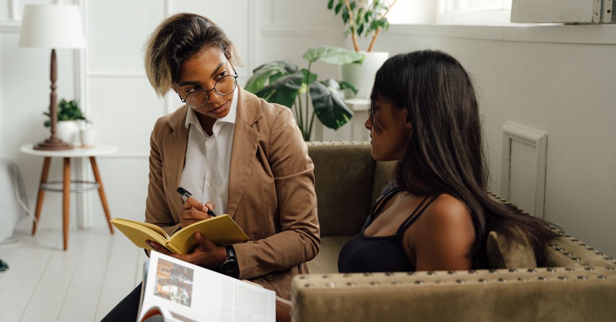A student having a focused conversation with a professor in an office, with papers and books visible