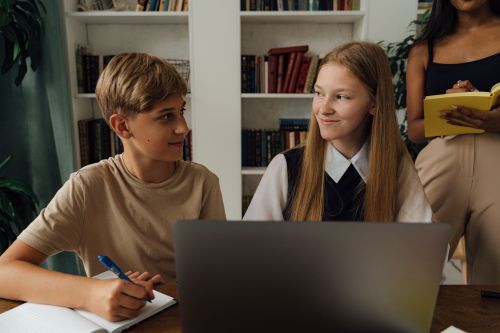 Free Group of teenagers studying together in a library setting, using a laptop and writing notes. Stock Photo
