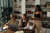 青少年学生在图书馆里使用笔记本电脑和书籍学习，注重团队合作与教育