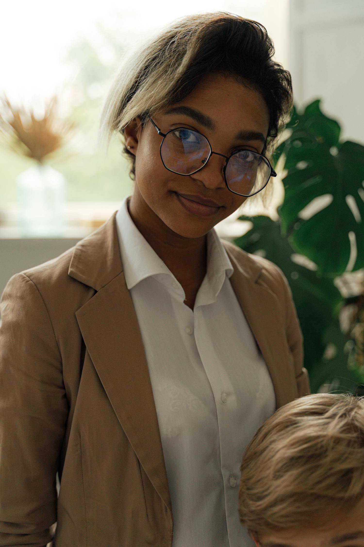 Confident woman wearing eyeglasses and a blazer, smiling in an office interior.