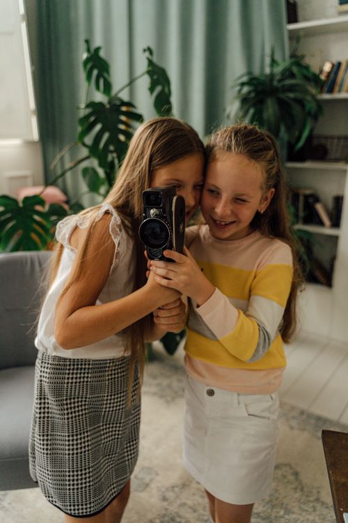 Free Charming photo of two young girls having fun with a vintage camera indoors. Stock Photo