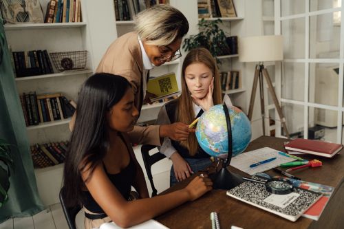 Free A teacher explaining geography to two students using a globe in a classroom setting. Stock Photo