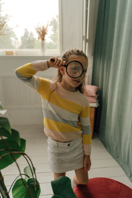 Free Young girl exploring indoors with a magnifying glass, embracing curiosity and discovery. Stock Photo