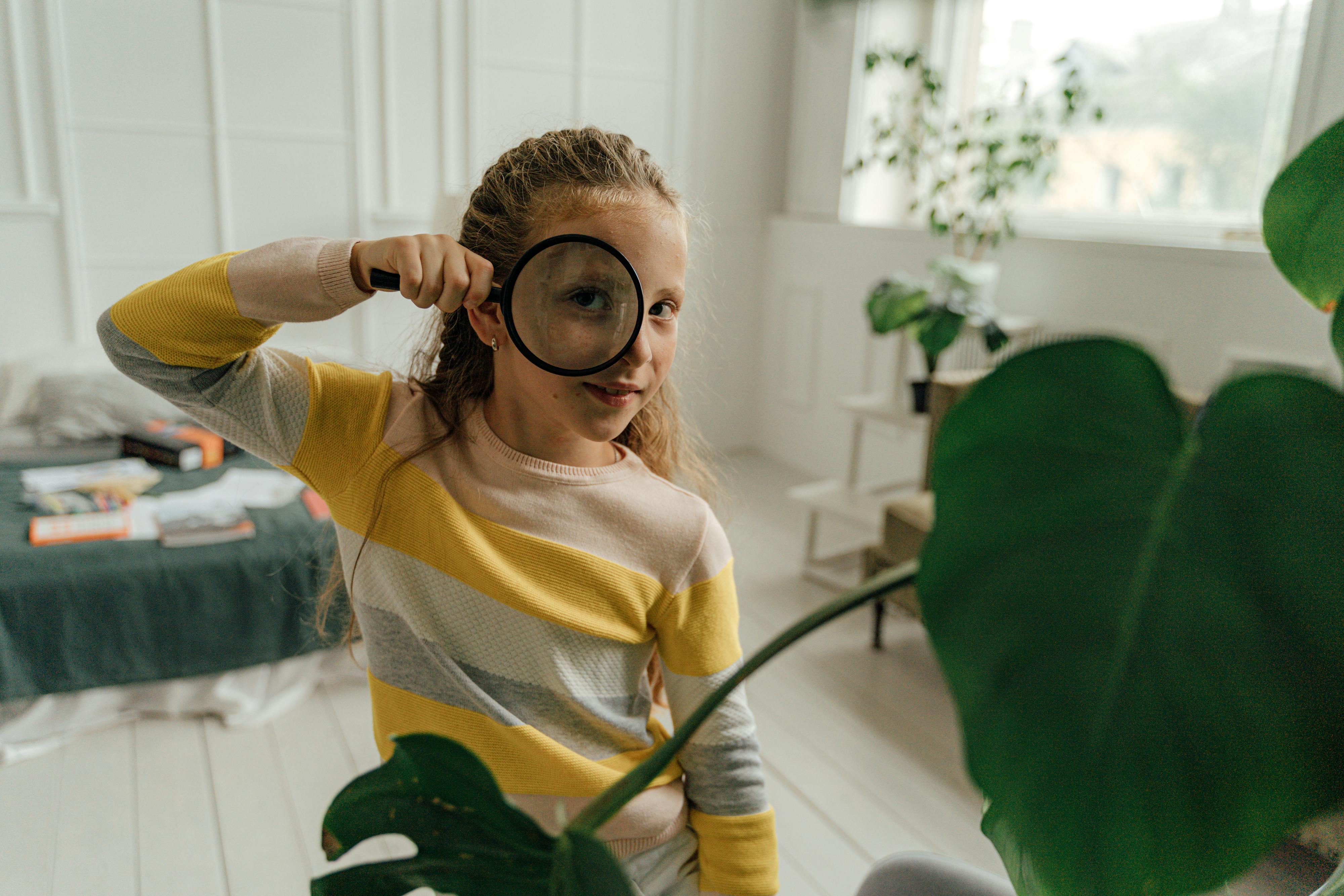 Curious child in a bright room examining the world with a magnifying glass.