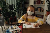 一位年轻女孩戴着口罩在笔记本上书写，适应着室内新常态