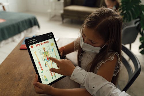 Free A Girl Wearing Face Mask Looking at the Screen of the Tablet  Stock Photo