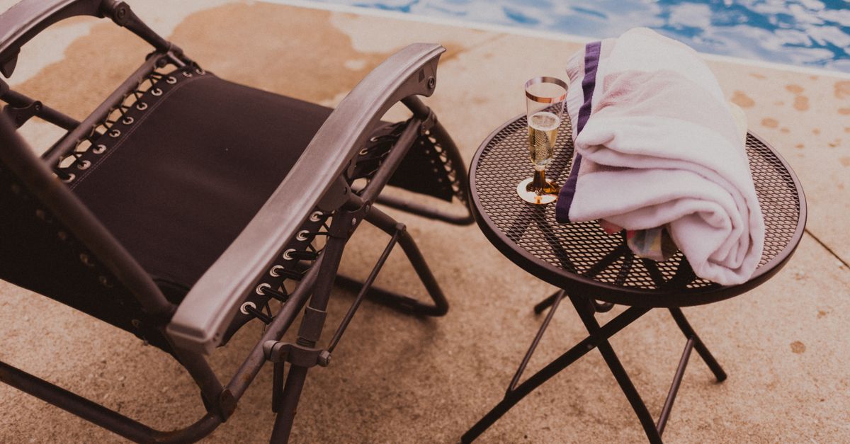 From above of comfortable deckchair and small round table with towel and glass of champagne near swimming pool