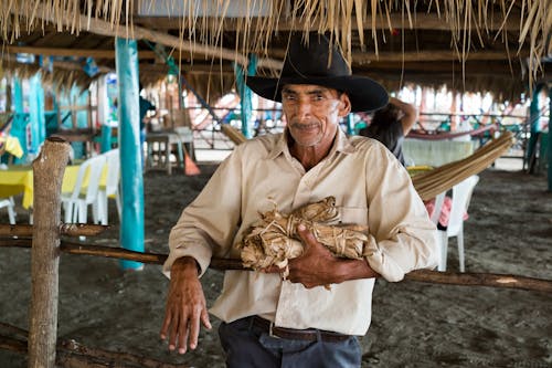 An Elderly Man in Black Cowboy Hat Leaning by the Wooden Fence while Looking at the Camera