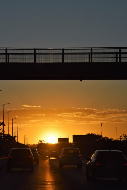 Free Silhouetted cars drive on a highway under a bridge during a vibrant sunset in Brasília, Brazil. Stock Photo