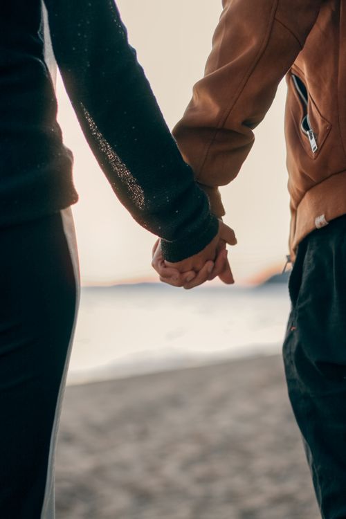 Free A couple holds hands during a romantic beach walk at sunset, symbolizing connection and love. Stock Photo