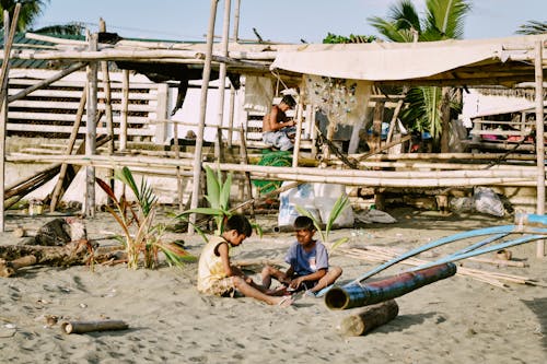 Boys Sitting on Beach Shore near Wooden Construction