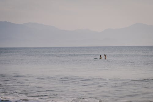 Mountain Silhouette Behind Two Men Surfing on Sea