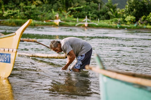 Man in Gray T-shirt Fishing Near Boats