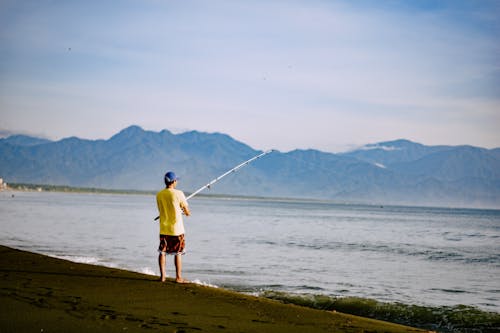 Man in Yellow Shirt Fishing in Sea near Mountains