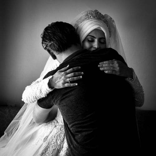 Free A heartfelt embrace between a bride in a wedding gown and her groom, captured in black and white. Stock Photo