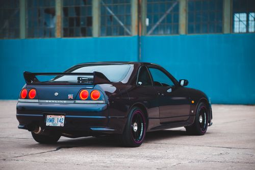 Free Black sports auto with bright taillights and license plate on rear bumper parked near old building Stock Photo