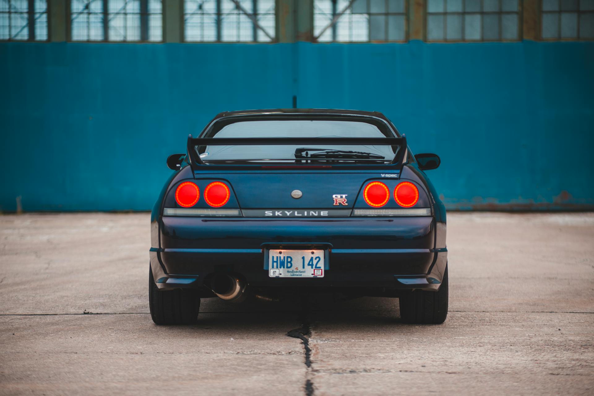 Bright taillights and license plate on rear bumper of luxury automobile parked on pavement near building