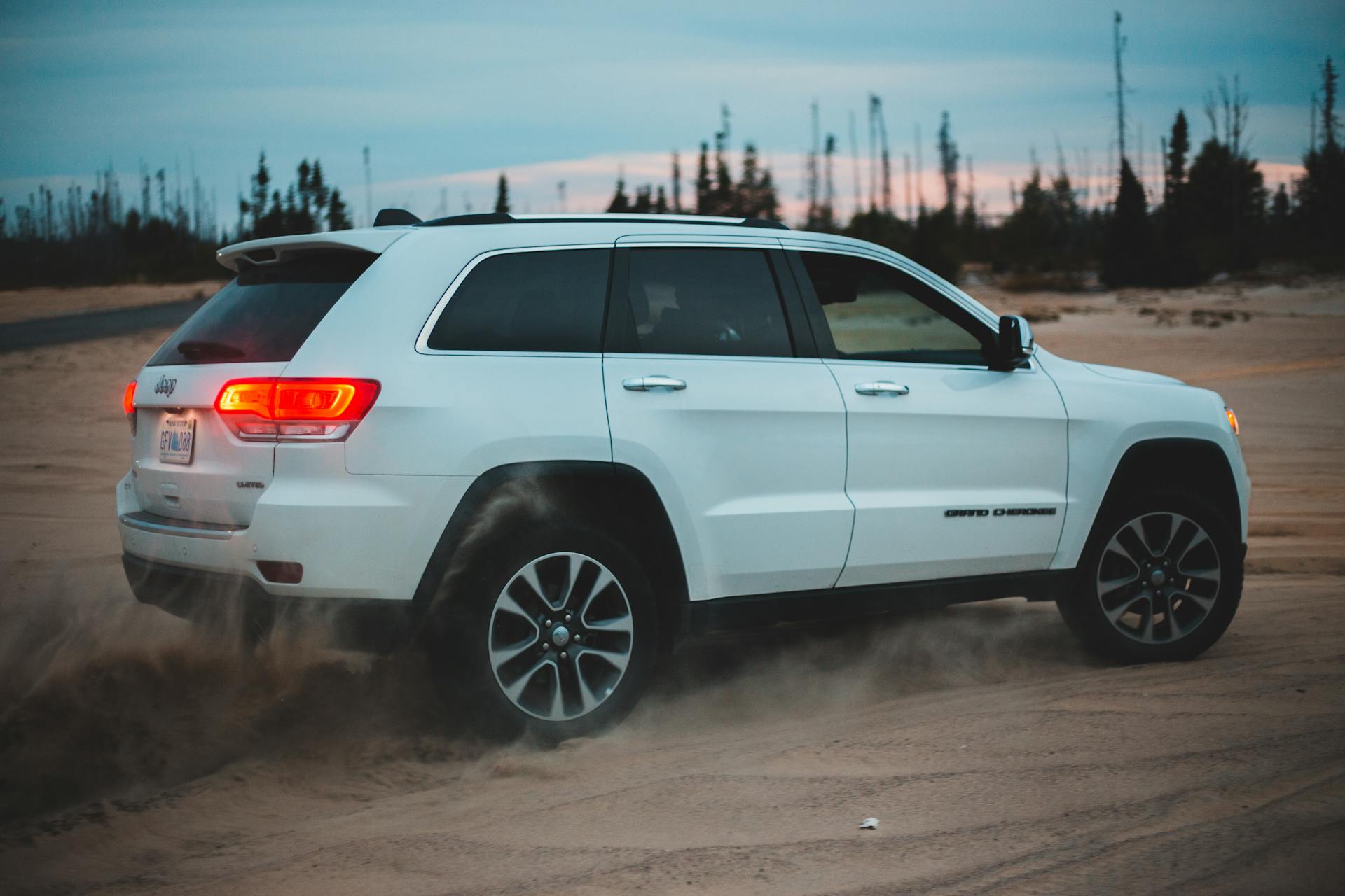 A white SUV navigating sandy terrain at dusk, showcasing off-road capabilities and modern design.