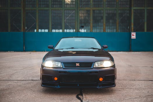 Luminous headlights of luxury black automobile parked on pavement near industrial building in daylight