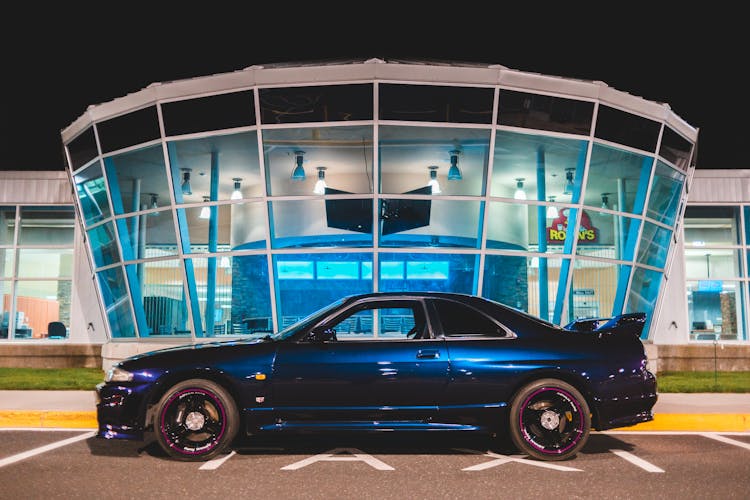 Sports Car On Road Near Modern Building In Evening