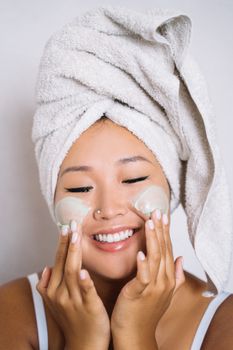 Smiling woman with a towel on her head applying cream to her face.
