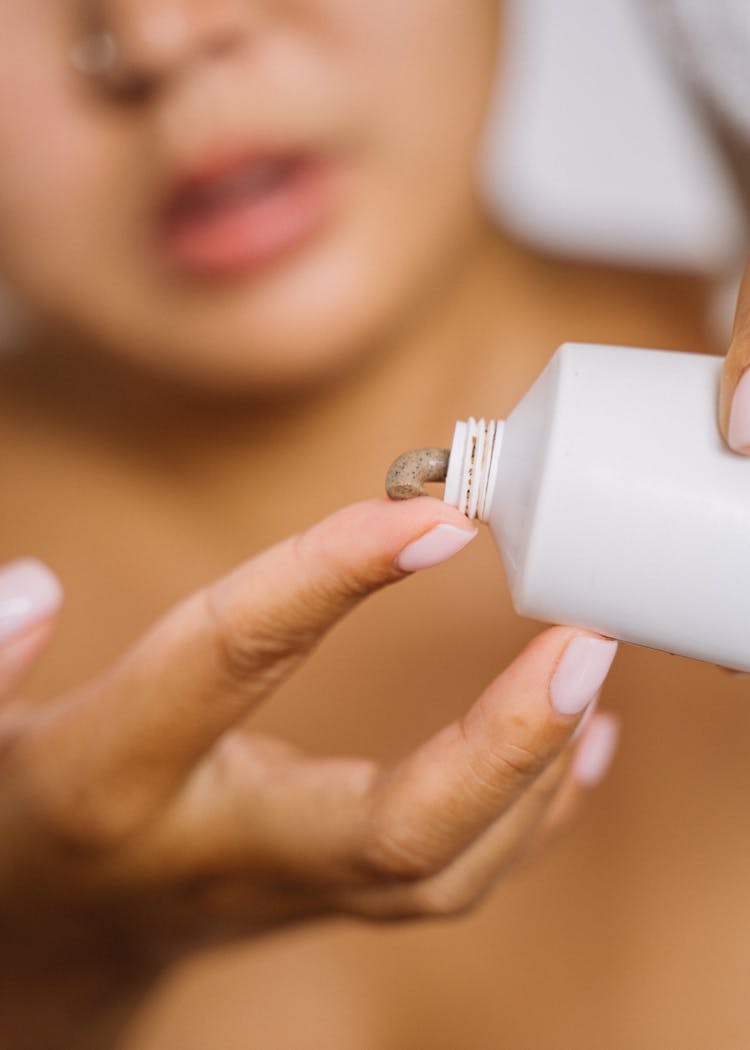 Close-up Of Person Putting Brown Cream On Finger 