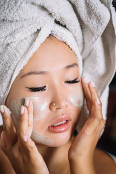 Close-up of a woman enjoying a skincare routine with facial cream and towel wrapped head.
